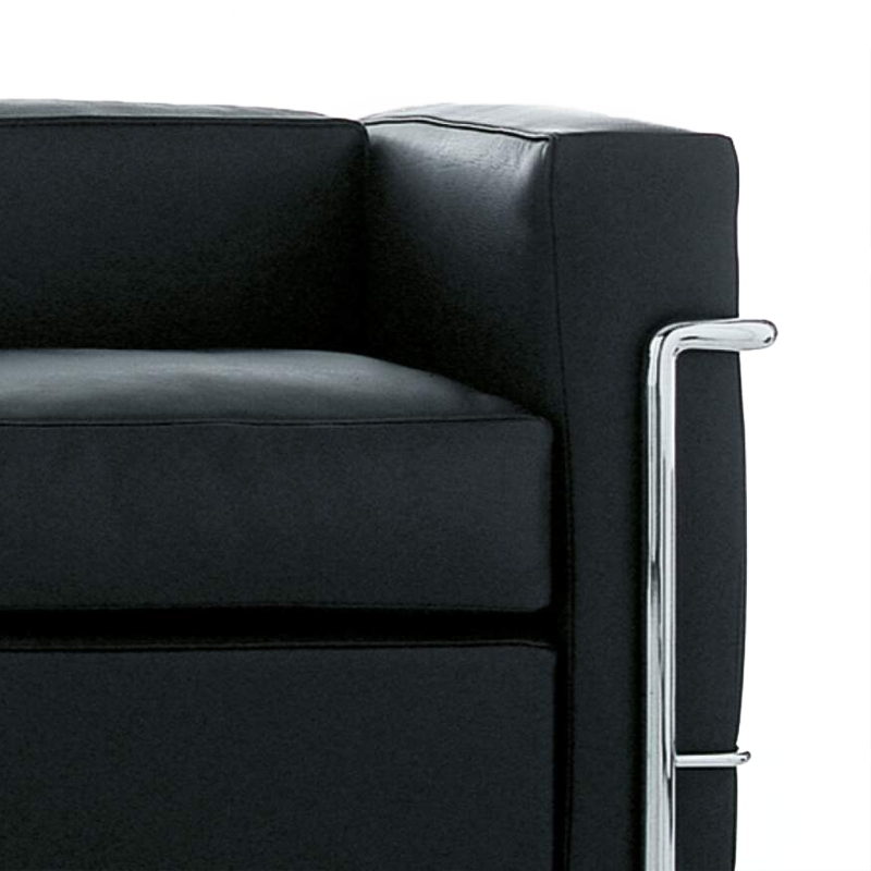 Gros plan sur l'accoudoir rembourré en cuir noir et les tubes chromés du canapé LC2 Cassina