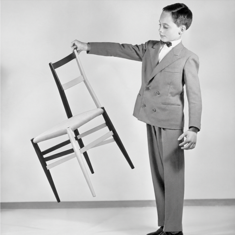 Photographie en noir et blanc d'un jeune homme soulevant la chaise Superleggera 699, célèbre pour son extrême légèreté