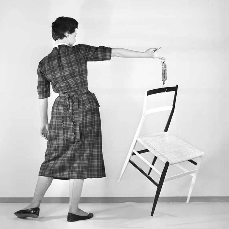 Photographie en noir et blanc montrant une femme soulevant une chaise Superleggera de Gio Ponti