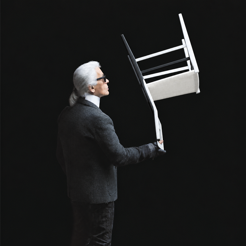 Karl Lagerfeld tenant une chaise Superleggera de Cassina d'une seule main sur un fond sombre