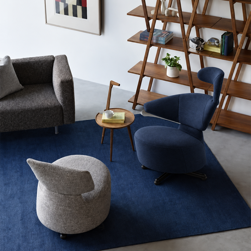 Fauteuil Canta bleu foncé de Toshiyuki Kita dans un salon contemporain avec canapé gris, tapis bleu et bibliothèque en bois