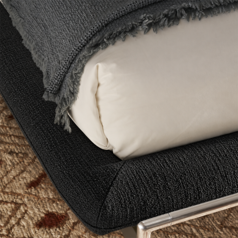 Gros plan sur le cadre rembourré en tissu noir du lit Esosoft Cassina avec linge de lit blanc et plaid à franges