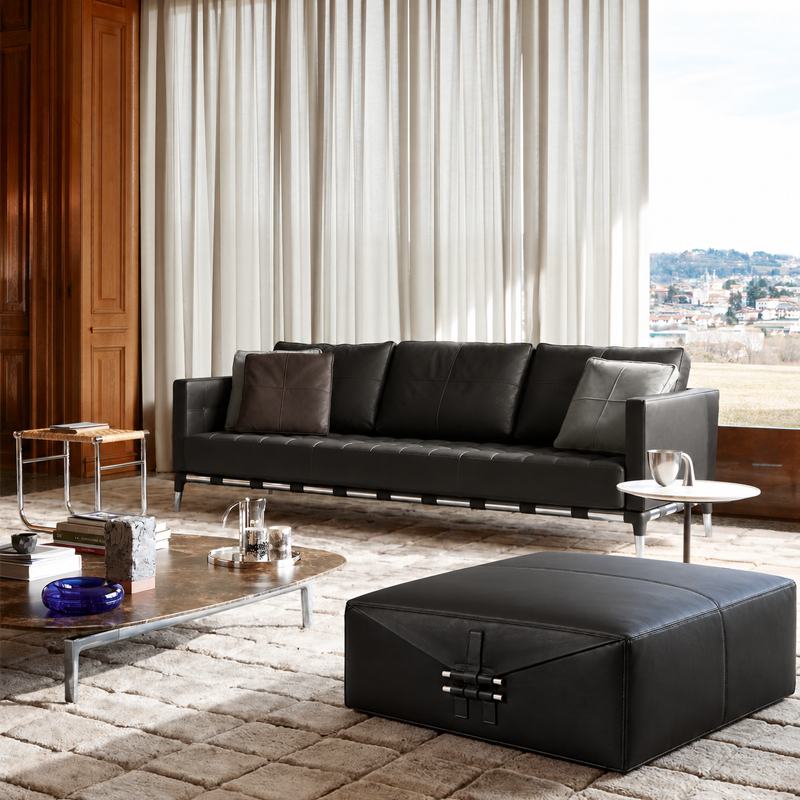 Pouf Somewhere El-S Cassina en cuir noir disposé devant un canapé contemporain dans un salon lumineux
