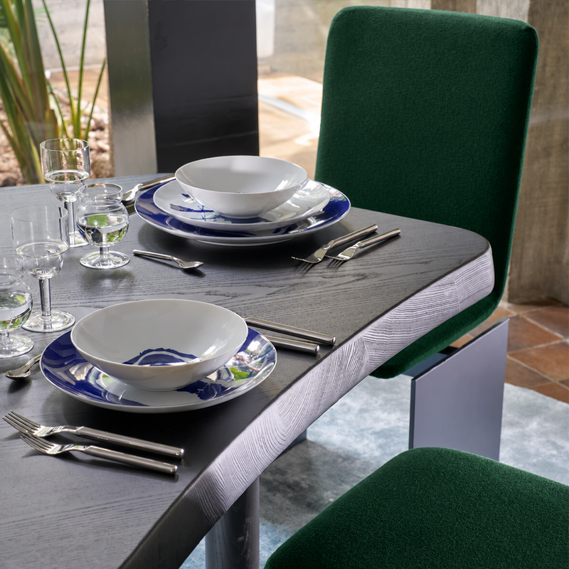 Détail de la table Montparnasse Cassina en frêne noir dressée pour un repas avec des chaises vertes