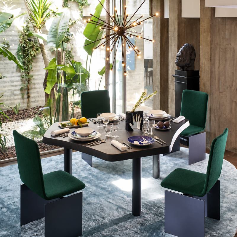 Table Montparnasse 545 de Charlotte Perriand entourée de chaises vertes dans une salle à manger contemporaine végétalisée