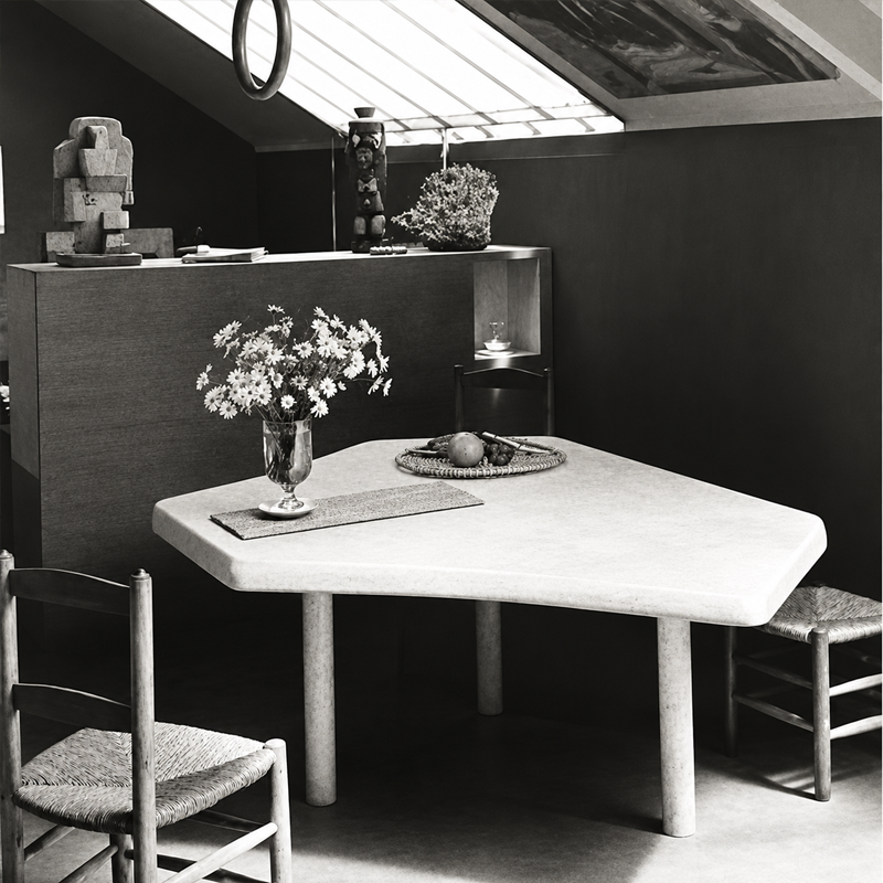 Photographie historique en noir et blanc montrant une table asymétrique entourée de chaises dans un intérieur d'époque