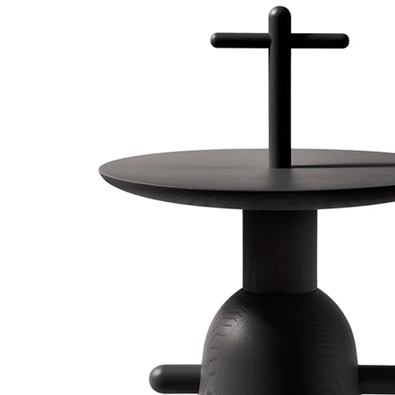 Gros plan sur le plateau rond en frêne teinté noir et la poignée en forme de croix de la table Réaction Poétique Cassina