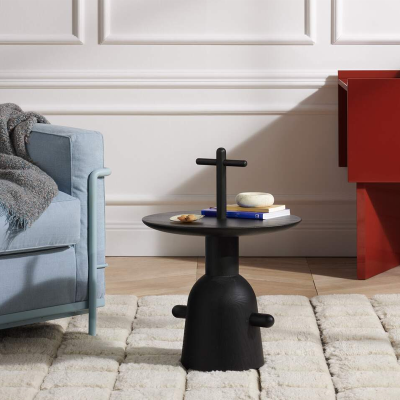 Table d'appoint Réaction Poétique noire de Jaime Hayon près d'un canapé bleu clair et d'un meuble rouge